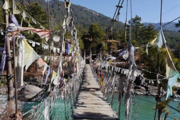 Brücke mit Gebetsfahnen in Bumthang mit Bergen im Hintergrund