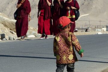 Gruppe von Nonnen in roter Tracht begegnen einem kleinen Jungen mit Mütze auf der Straße in Ladakh