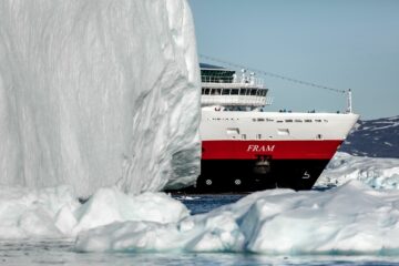 Schiff mit rot-schwarzem Bug fährt an riesigem Eisblock vorbei