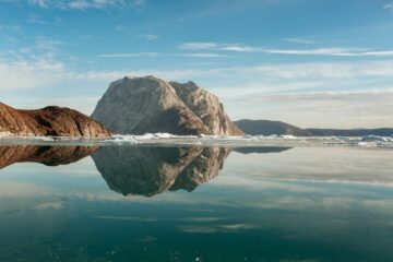 Graue Berge spigeln sich im türkisblauen Wasser