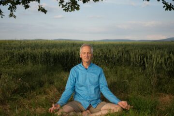 Mann meditiert auf Wiese im Lotussitz