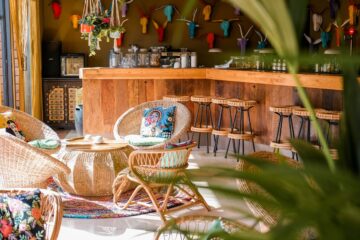 Lounge-Bereich mit Rattanmöbeln an Holztheke und bunten Gypsy-Kissen mit Frauenportraits