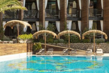 Pool mit Palm-Sonnenschirmen und kleinen Balkonen am Hauptgebäude