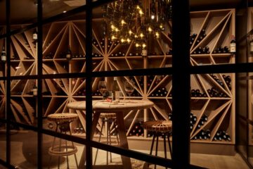 Regal mit Weinen und Tisch mit zwei Rattan-Barhockern