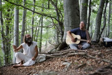 Zwei Männer singen mit Gitarre unter den Bäumen