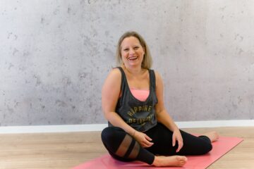 Lachende Trainerin auf Yoga-Matte