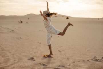 Frau tanzt mit Sonnenhut im Sand