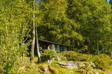 Hütte im grünen Wald mit Personen auf Veranda