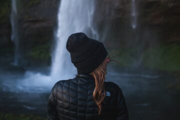 Frau mit Mütze in Rückenansicht vor Wasserfall
