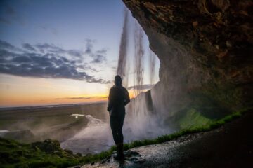 Frau hinter Wasserfall bei Sonnenuntergang