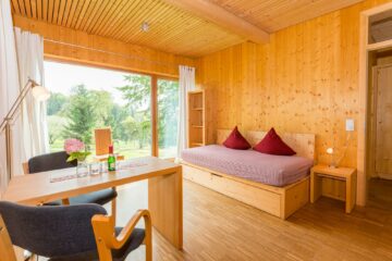 Zimmer aus Holz mit Einzelbett und Tisch mit Stühlen