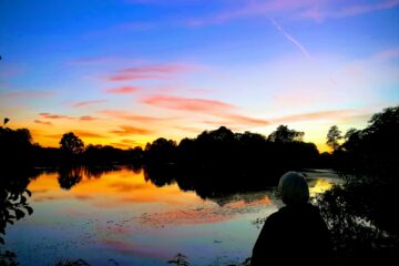 Frau sitzt am See bei Sonnenuntergang