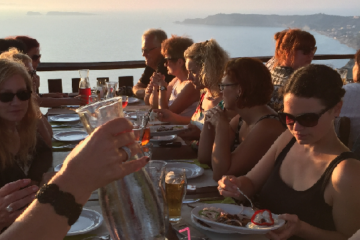 Gruppe sitzt auf Terrasse am Meer und isst zu Abend
