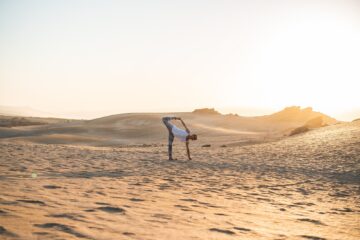 Yogapose mit Bein in den Himmel und Hand in den Sand