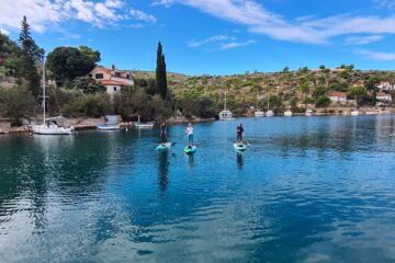 Gruppe auf SUP an Küstenline mit Häusern und Booten