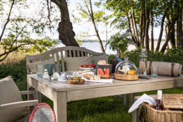 Bank am See mit Picknickkorb und Decke und Proviant auf dem Tisch