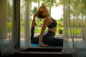 Frau sitzend in yoga-Pose hinter Vorhängen auf Terrasse