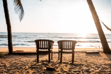 Zwei Stühle am Strand zwischen zwei Palmen mit Blick zum Meer