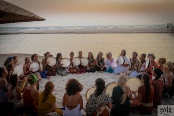 Gruppe sitzt im Sand am Meer mit Trommeln