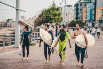 Gruppe mit Surfbrettern im Arm läuft Promenade entlang