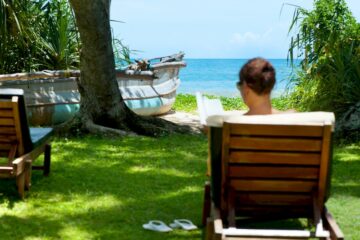 Eine Frau sitzt in einem Stuhl im Garten, unter Palmen mit Blick auf den indischen Ozean