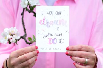 Frau hält eine Spruchkarte in die Kamera mit den Worten 'If you can dream it, you can do it.'