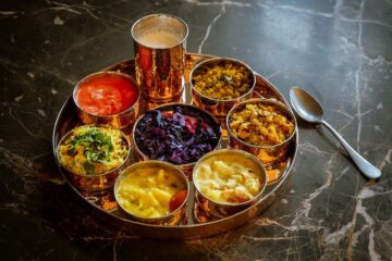 Traditionelles indisches Thali – Auswahl verschiedener vegetarischer Gerichte, die auf einem runden Metalltablett (Thali) in kleinen Schälchen serviert werden.