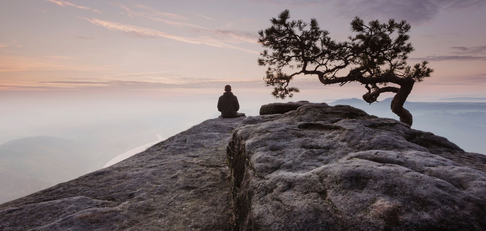 Mann in Rückenansicht in Meditationspose, der auf einer Steinküste sitzt, als Symbol für Meditationsreisen